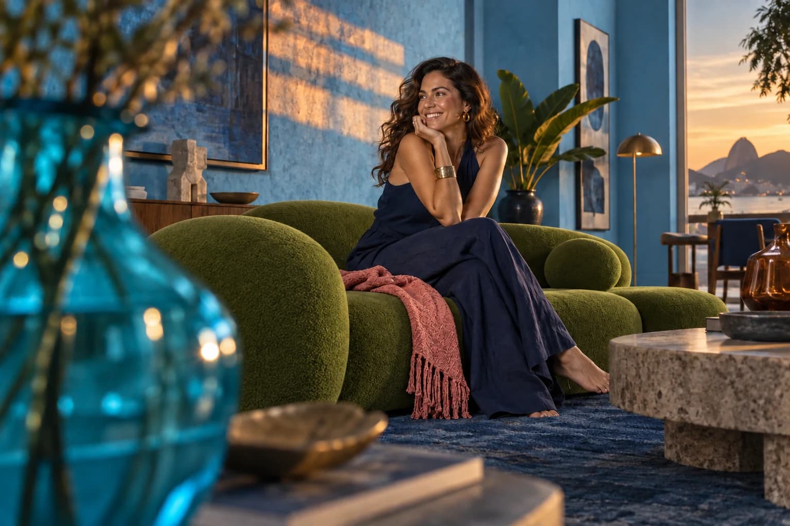 Mulher sentada em poltrona em uma sala azul com luz quente e vista ao entardecer.